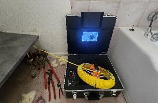 Valise de caméra d'inspection vidéo ouverte avec son câble jaune, posée au sol d'une salle de bain près d'une baignoire