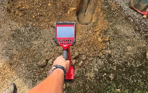 Technicien tenant un appareil de détection rouge au-dessus d'une fouille remplie d'eau