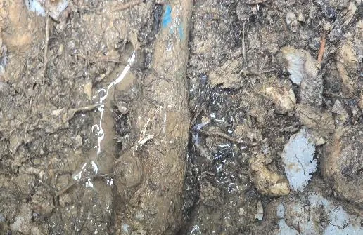 Fuite d'eau visible sur une canalisation enterrée dans une fouille de terre humide
