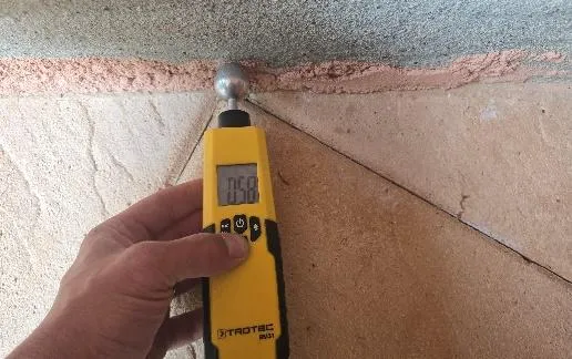 Main tenant un humidimètre jaune contre l'angle d'un mur pour mesurer le taux d'humidité